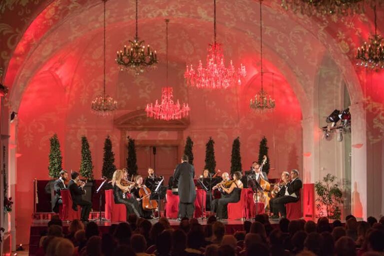 Orchestra performing in elegant, red-lit hall.